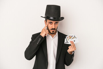 Young magician man holding a magic card isolated on white background pointing temple with finger, thinking, focused on a task.