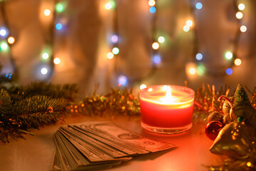 Money with a burning candle on a Christmas background with a glowing garland.