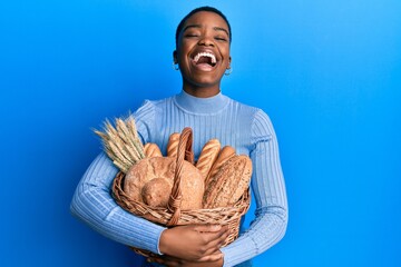 Young african american woman holding wicker basket with bread smiling and laughing hard out loud...