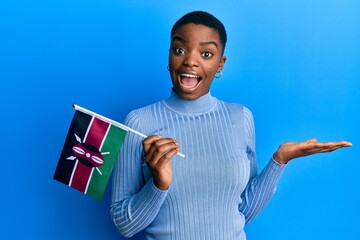 Young african american woman holding kenya flag celebrating achievement with happy smile and winner...