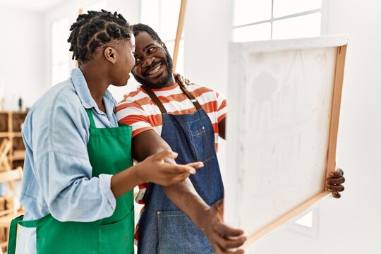 African american painter couple smiling happy holding canvas at art studio.