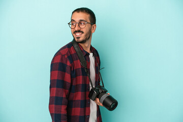 Young caucasian photographer man isolated on blue background looks aside smiling, cheerful and pleasant.