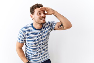 Fototapeta premium Handsome young man standing over isolated background very happy and smiling looking far away with hand over head. searching concept.