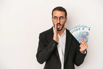 Young caucasian business man holding banknotes isolated on white background is saying a secret hot braking news and looking aside