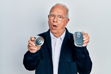 Senior man with grey hair holding canned food in shock face, looking skeptical and sarcastic,...