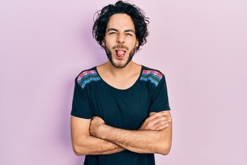 Handsome hispanic man with arms crossed gesture sticking tongue out happy with funny expression.