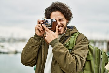 Handsome hispanic man using vintage camera by marina port