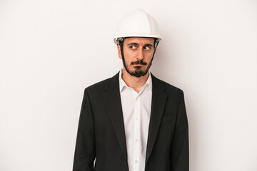 Young architect man wearing a construction helmet isolated on white background confused, feels doubtful and unsure.