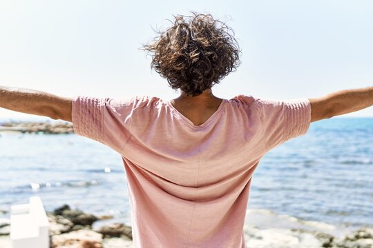 Young Hispanic Man On Back View Breathing With Arms Open At The Beach.