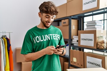 Young arab man wearing volunteer uniform using smartphone at charity center