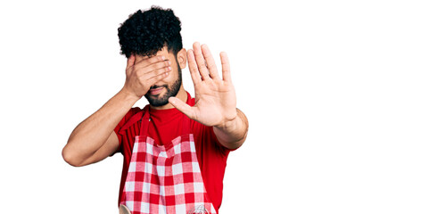 Young arab man with beard wearing cook apron covering eyes with hands and doing stop gesture with sad and fear expression. embarrassed and negative concept.