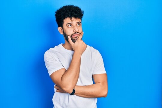 Young arab man with beard wearing casual white t shirt thinking worried about a question, concerned and nervous with hand on chin