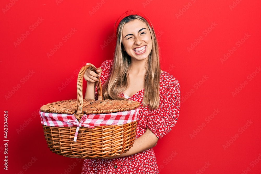 Poster beautiful hispanic woman holding picnic wicker basket winking looking at the camera with sexy expres