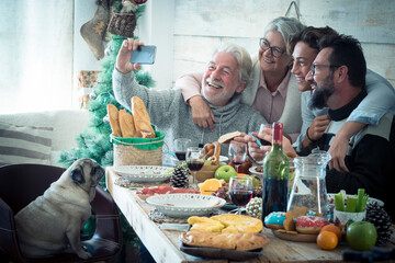 Senior man taking selfie using mobile phone with family on dining table with pet dog sitting on...