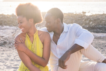 African american couple sitting and relaxing on beach by sea. Happy black couple spending quality time outdoors. African american man and woman enjoying sitting on sand at beach.