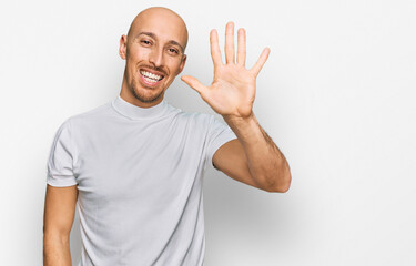 Bald man with beard wearing casual white t shirt showing and pointing up with fingers number five while smiling confident and happy.