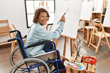 Middle age hispanic disabled artist woman drawing sitting on wheelchair at art studio.