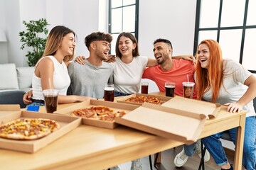 Group of young people smiling happy and hugging eating italian pizza at home.