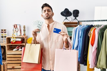Young hispanic man holding shopping bags and credit card looking at the camera blowing a kiss being lovely and sexy. love expression.