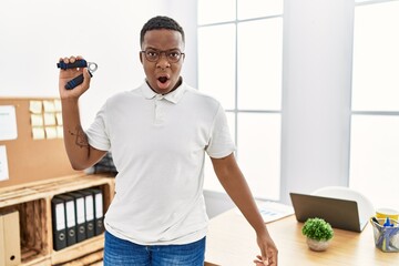 Young african man training muscle with hand grip at office scared and amazed with open mouth for surprise, disbelief face