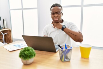 Young african man working at the office using computer laptop cutting throat with hand as knife, threaten aggression with furious violence