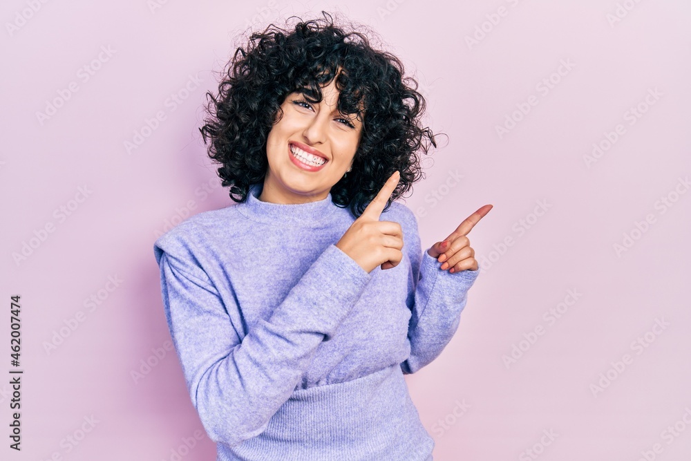 Sticker young middle east woman wearing casual clothes smiling and looking at the camera pointing with two h