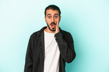 Young caucasian man isolated on blue background shouts loud, keeps eyes opened and hands tense.