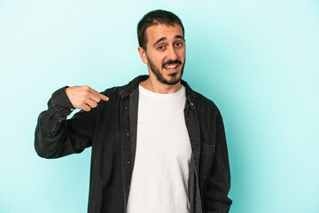 Young caucasian man isolated on blue background person pointing by hand to a shirt copy space, proud and confident