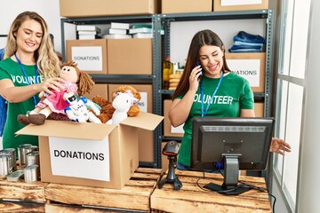 Two young volunteers woman smiling happy working at charity center. Girl smiling happy talking on the smartphone.