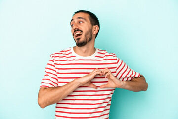 Young caucasian man isolated on blue background smiling and showing a heart shape with hands.