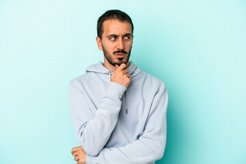 Young caucasian man isolated on blue background looking sideways with doubtful and skeptical expression.