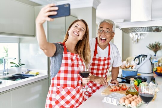Middle age hispanic couple smiling happy cooking and make selfie by the smartphone at the kitchen.