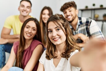 Group of young friends smiling happy make selfie by the smartphone sitting on the sofa at home.