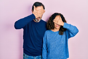 Middle age couple of hispanic woman and man hugging and standing together covering eyes with hand,...