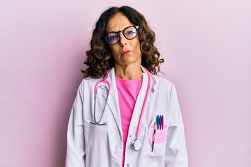 Middle age hispanic woman wearing doctor uniform and glasses relaxed with serious expression on face. simple and natural looking at the camera.