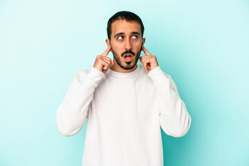 Young caucasian man isolated on blue background covering ears with fingers, stressed and desperate by a loudly ambient.