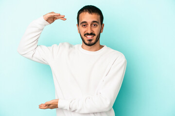 Fototapeta premium Young caucasian man isolated on blue background holding something little with forefingers, smiling and confident.
