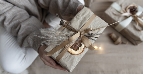 Close-up of a Christmas gift box, decorated in craft style, in female hands.