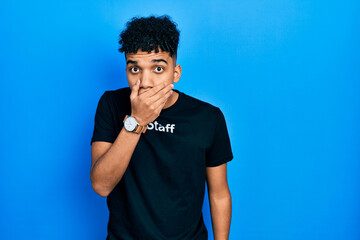 Young african american man wearing staff t shirt shocked covering mouth with hands for mistake....