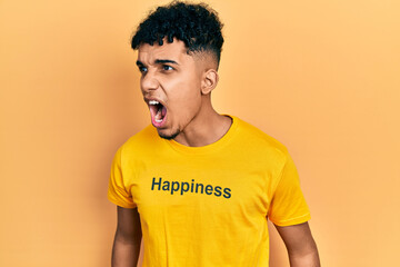 Young african american man wearing t shirt with happiness word message angry and mad screaming frustrated and furious, shouting with anger. rage and aggressive concept.