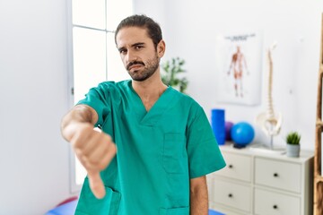 Young physiotherapist working at pain recovery clinic looking unhappy and angry showing rejection...
