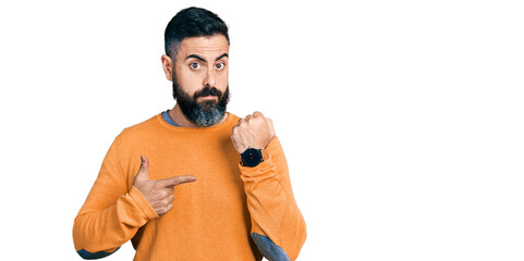 Hispanic man with beard wearing casual winter sweater in hurry pointing to watch time, impatience,...