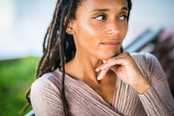 Fototapeta na wymiar Thoughtful african american woman with hand on chin. Black woman with deadlocks hairstyle. Dreamy young black woman looking away, resting chin on hand. Woman with unsure facial expression 