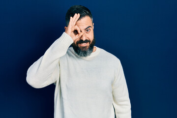 Young hispanic man wearing casual clothes doing ok gesture with hand smiling, eye looking through fingers with happy face.