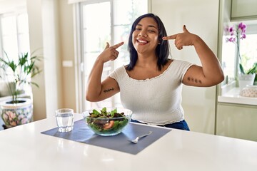 Obraz na płótnie Canvas Young hispanic woman eating healthy salad at home smiling cheerful showing and pointing with fingers teeth and mouth. dental health concept.