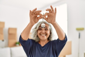 Middle age grey-haired woman smiling happy holding key of new home.