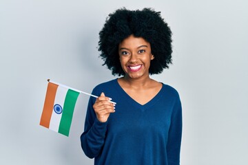 Young african american woman holding india flag looking positive and happy standing and smiling with a confident smile showing teeth