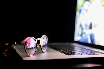 Glasses near the laptop, reflect light from the screen in the dark, copy space.
