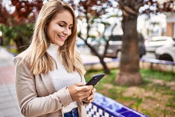 Young blonde woman smiling confident using smartphone at park