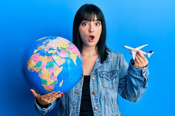 Fototapeta premium Young hispanic woman holding paper toy and world ball afraid and shocked with surprise and amazed expression, fear and excited face.